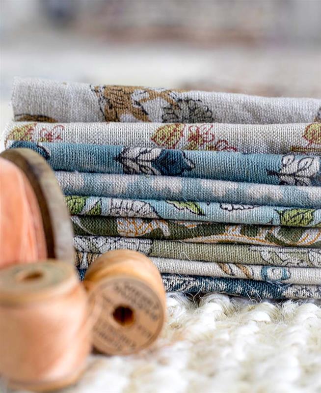 A stack of 220 GSM solid linen and block-printed cotton fabric rolls, showcasing the heavy drape and vibrant mineral-dyed colors for professional textile projects.