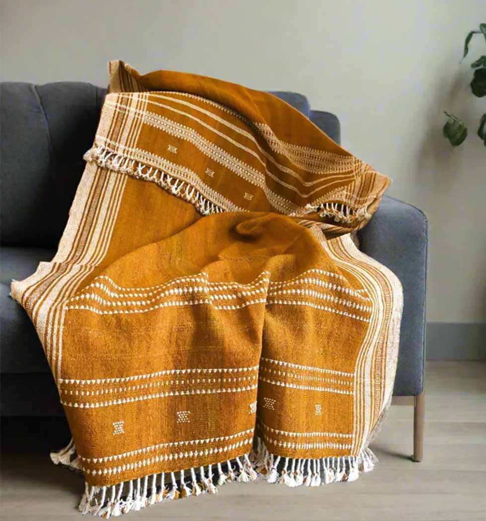 Orange patterned throw blanket draped over a gray sofa against a neutral wall.