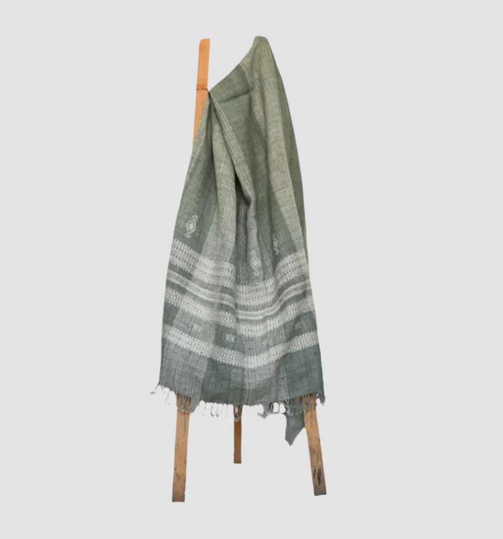Green and white patterned towel draped over a wooden rack on a light gray background