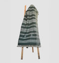 Green and white striped blanket draped over a wooden chair on a light gray background
