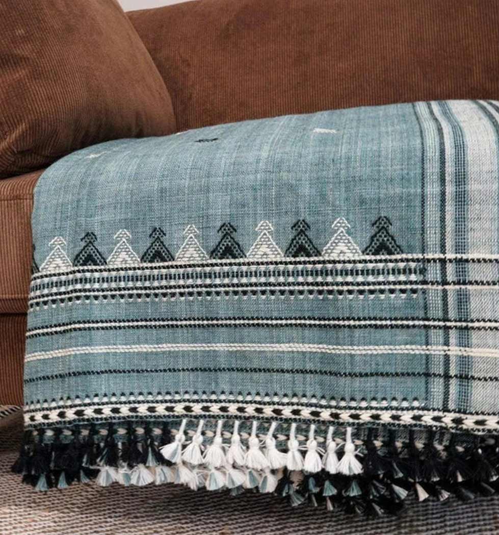 Textile with geometric pattern and tassels draped over a brown couch.