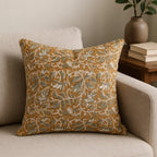 Mustard linen pillow cover with hand-blocked pale green floral vine pattern and brown outlines on a neutral sofa.
