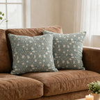 Hand block printed ice blue linen pillow covers featuring pale green botanical floral vines on a brown sofa.