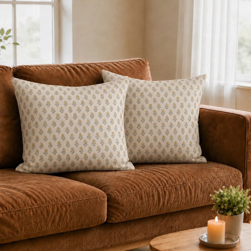 Two natural linen pillow covers featuring a hand-blocked lemon yellow and brown floral buti pattern on a brown sofa.