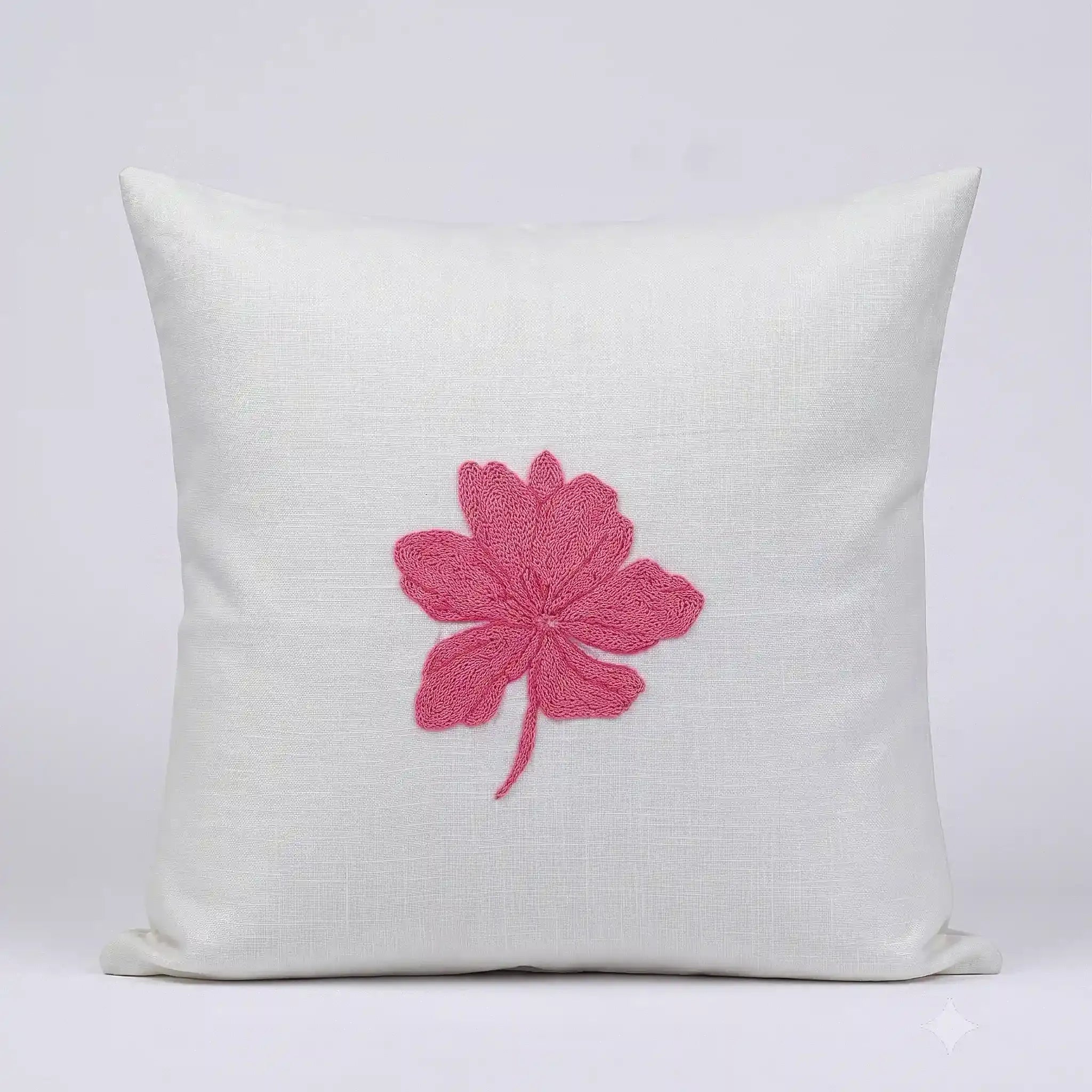 A square off-white linen throw pillow featuring a prominent pink embroidered hibiscus flower in the center, set against a clean light gray background.