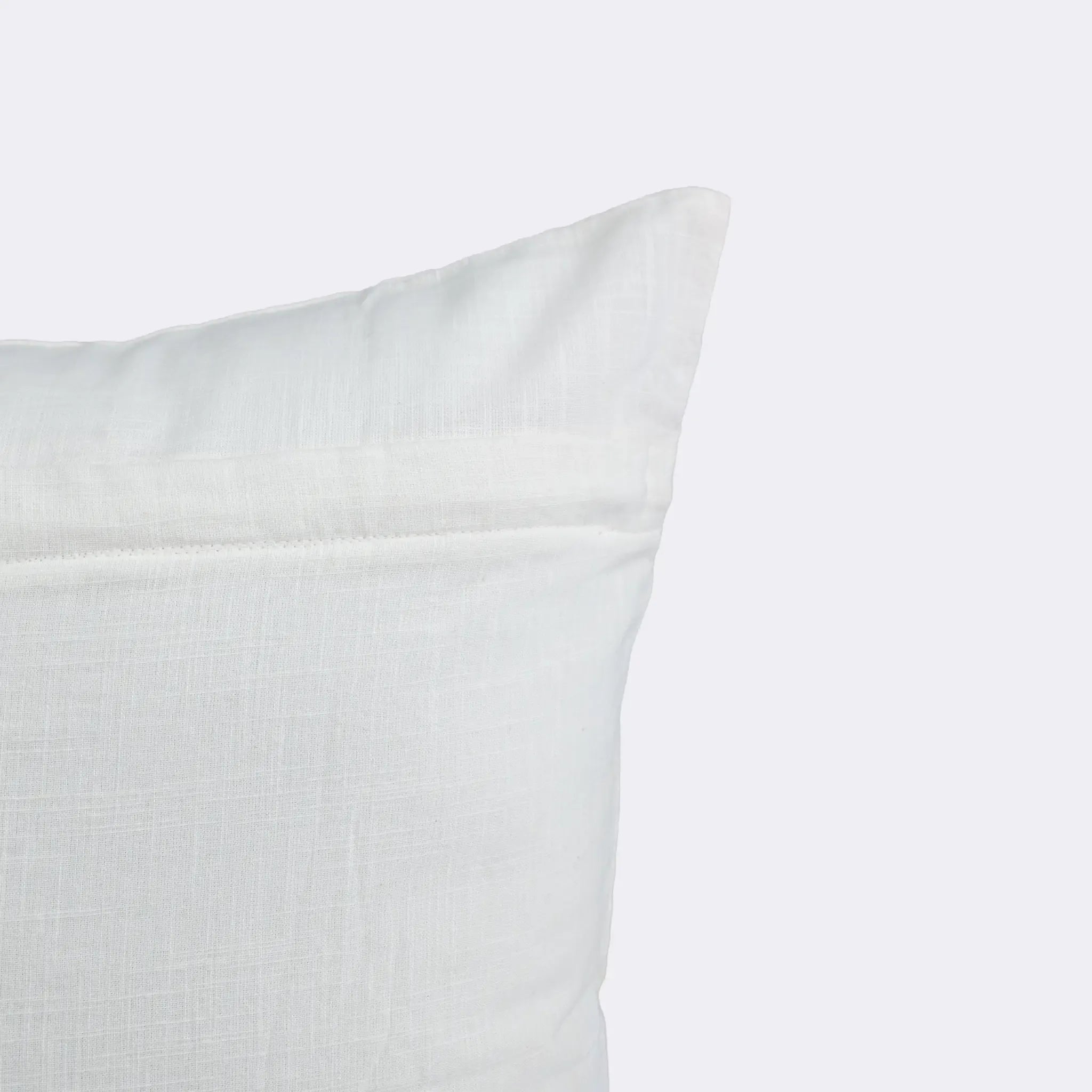 A close-up of a white textured throw pillow corner against a light gray background.