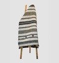 Textile with striped pattern draped over a wooden chair on a light gray background