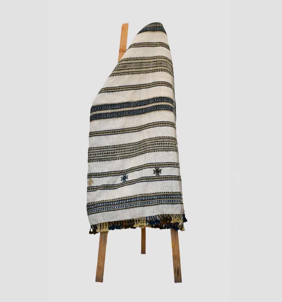Textile with striped pattern draped over a wooden chair on a light gray background
