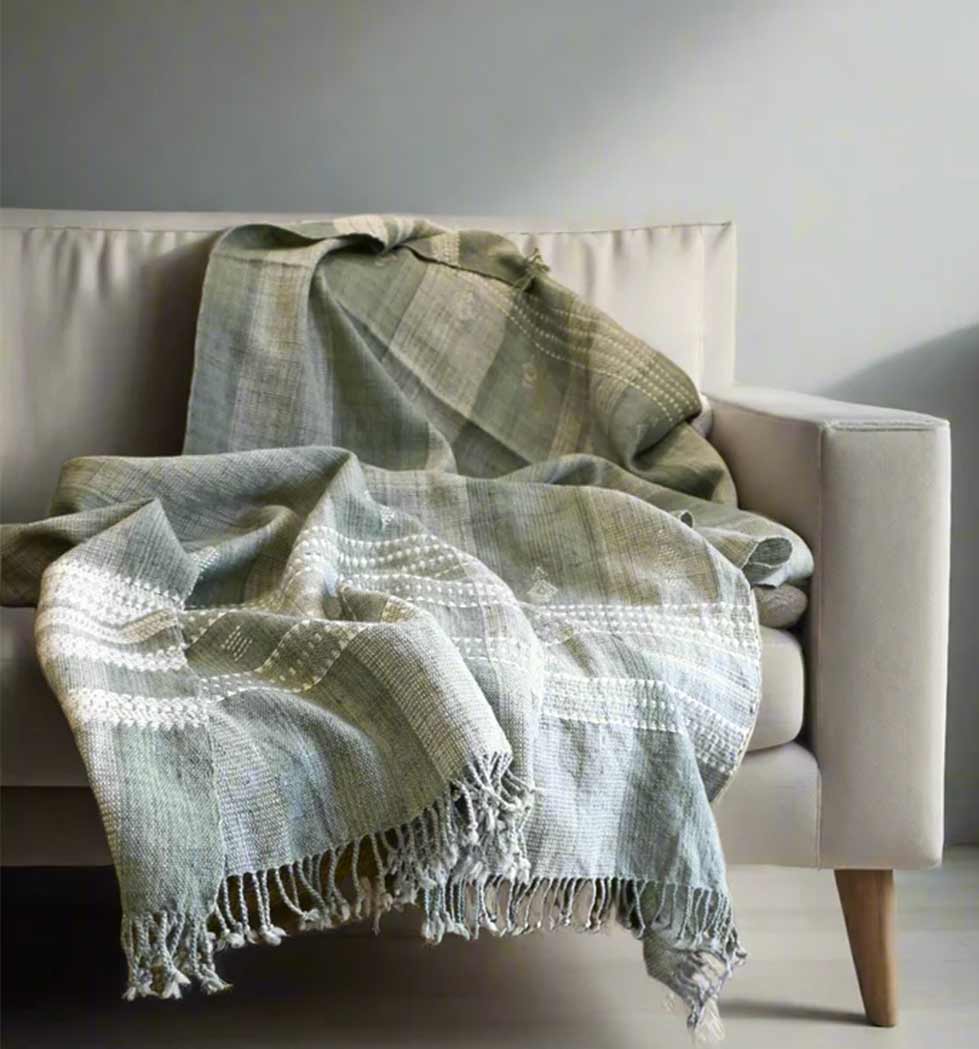 Green textured blanket draped over a beige sofa against a gray wall.