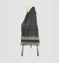 Textured blanket with tassels draped over a wooden chair on a light gray background