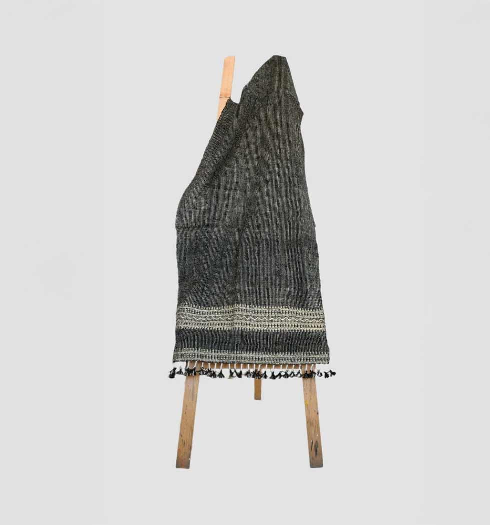Textured blanket with tassels draped over a wooden chair on a light gray background