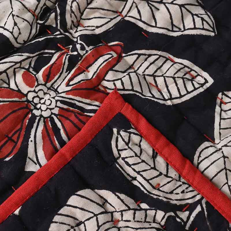 Close-up of a quilt with floral patterns in red, white, and black on a dark background.