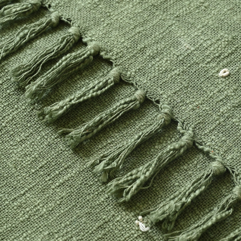 Close-up of a green embroidered blanket with tassels