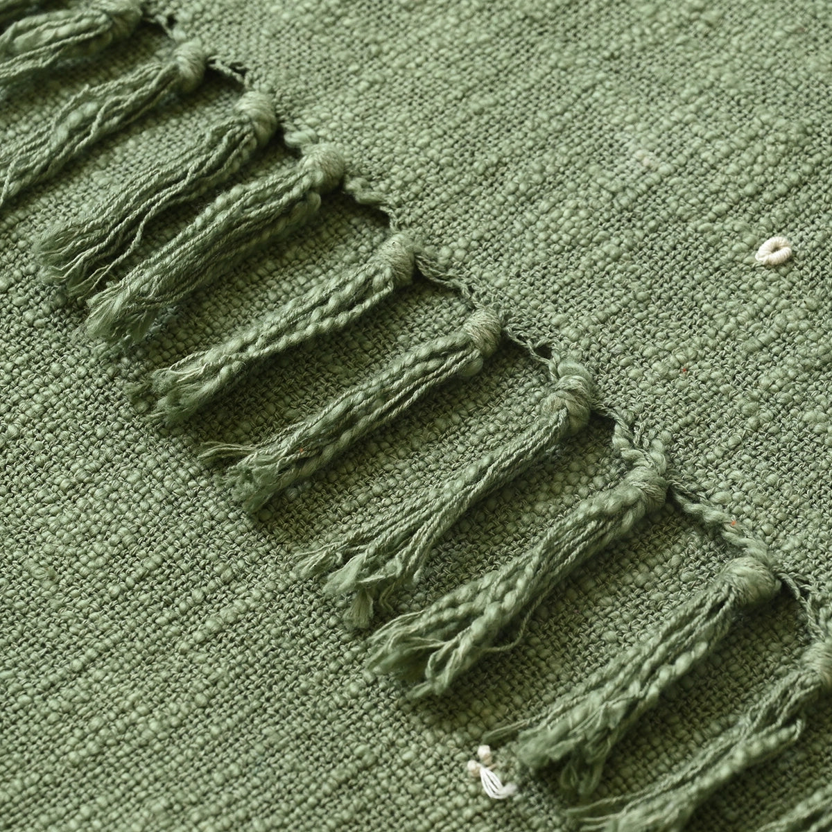 Close-up of a green embroidered blanket with tassels