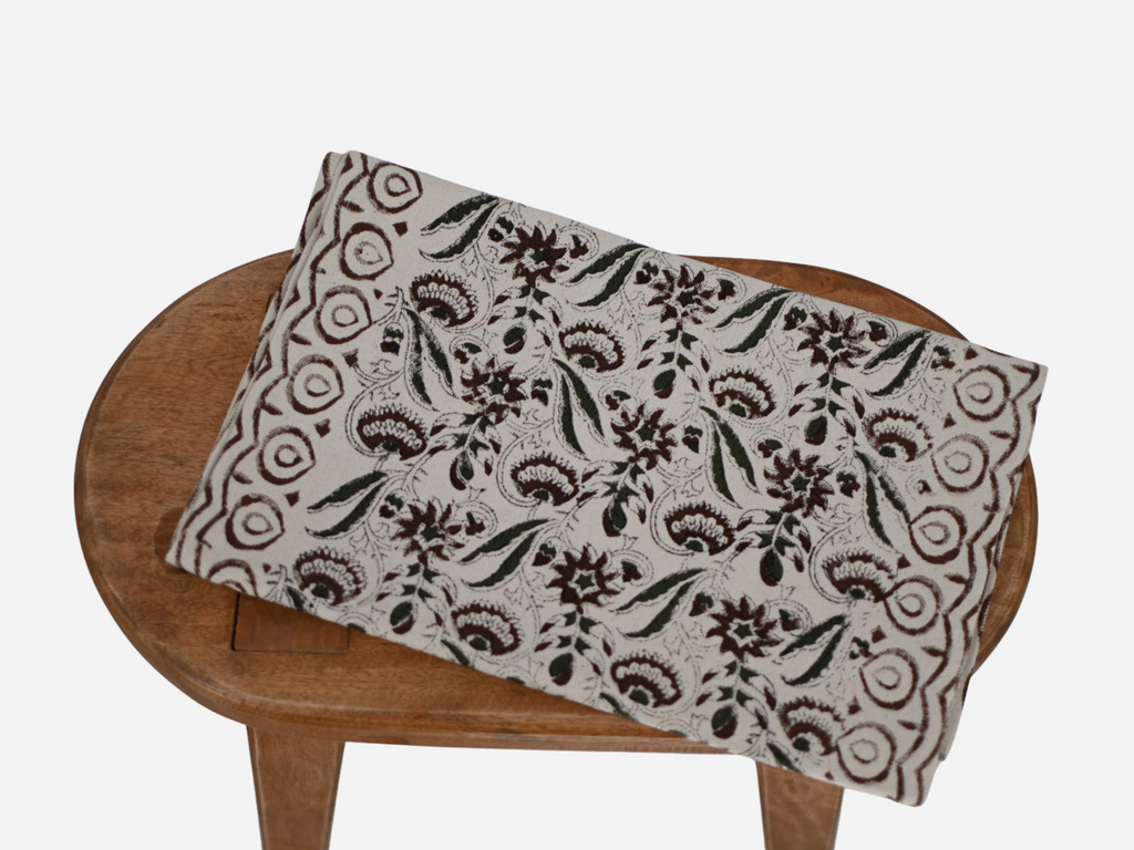 A beige cotton table runner with brown block print floral patterns displayed on a wooden table.